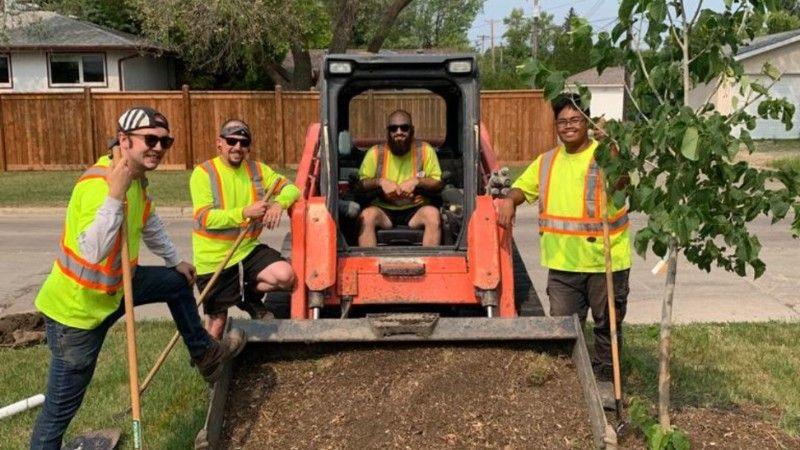 Green Drop crew posing with a loader and a freshly planted tree during a community project.